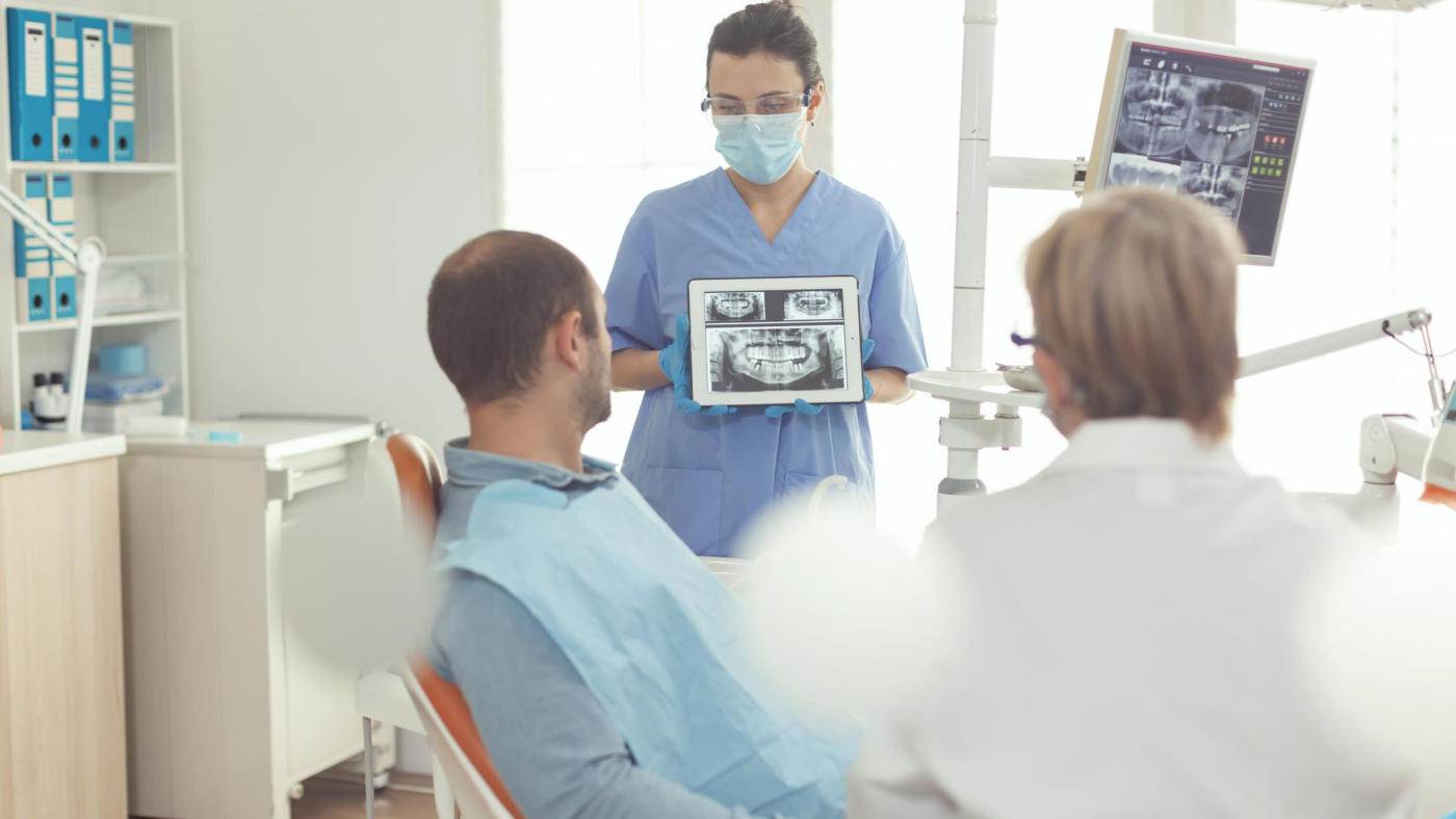 orthodontist-nurse-holding-digital-tablet-with-tooth-radiography-screen-explaining-sick-man-stomatology-treatment-prevent-toothache-patient-sitting-dental-chair-modern-dentistry-office
